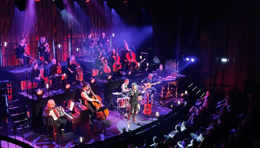 En orkester spelar på en scen i Stockholm, med en sångare i förgrunden. En levande revyupplevelse.