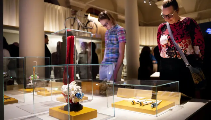 Besökare på muzeum nobla beundrar utställningar i glasmonter, inklusive en röd scarf och molekylmodeller.