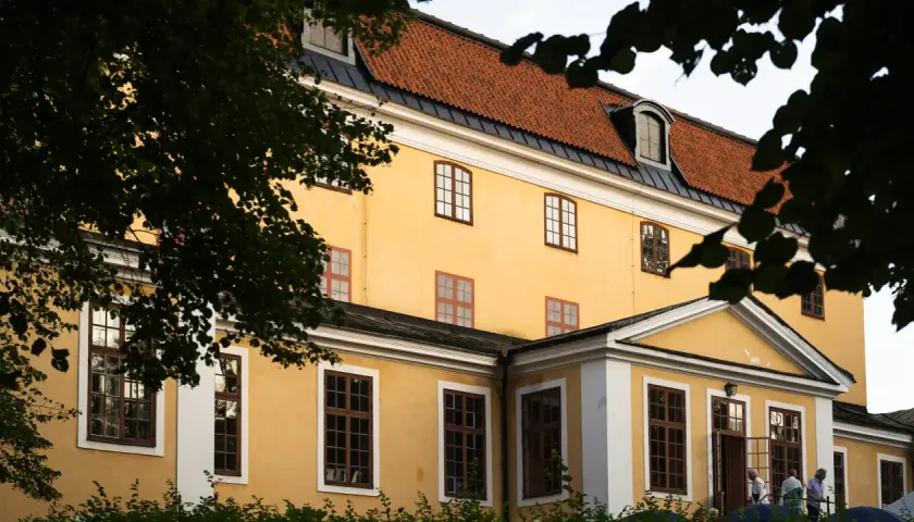 Gula fasaden på Ulriksdals teater med tegeltak och mörkgröna trädgrenar som ramar in.
