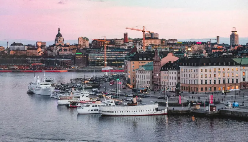 Vackert ljus över vattnet och båtar vid kajen i Stockholm. Staden ser inbjudande ut, redo för äventyr imorgon.