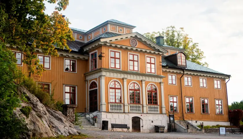 Vackert gul träbyggnad med röda fönster och tak, Rastaborgs slott, omgivet av höstfärgad grönska.