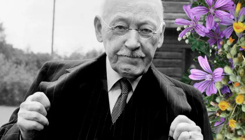 Äldre man med glasögon och mustasch, klädd i kostym. Bredvid honom en bukett med lila och gula blommor. Han är alfven som skrev.
