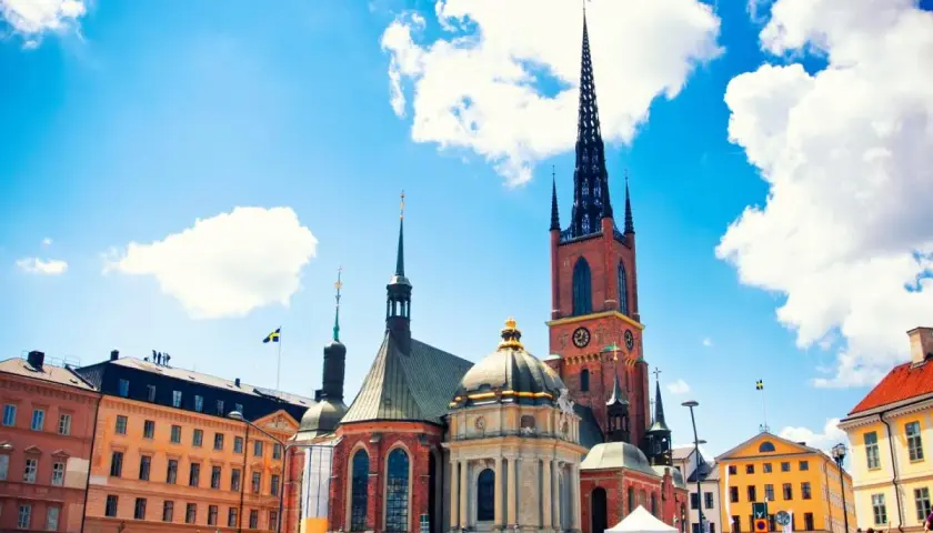 Stadshuset i Gamla Stan, Stockholm, med sina torn och en gul byggnad under en blå himmel med moln.