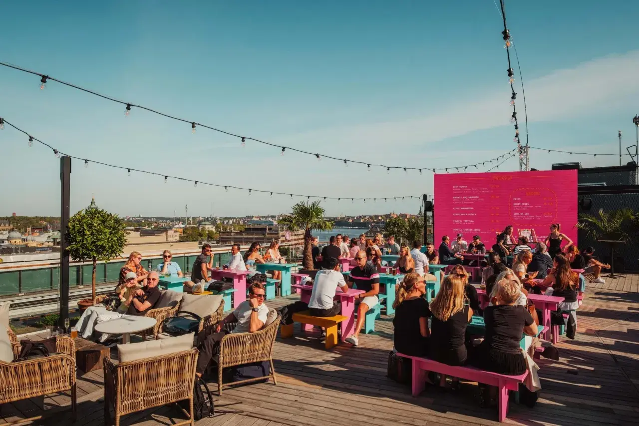 Folk njuter av solen och utsikten på en takbar i Stockholm. En perfekt plats för ett sommarevenemang.