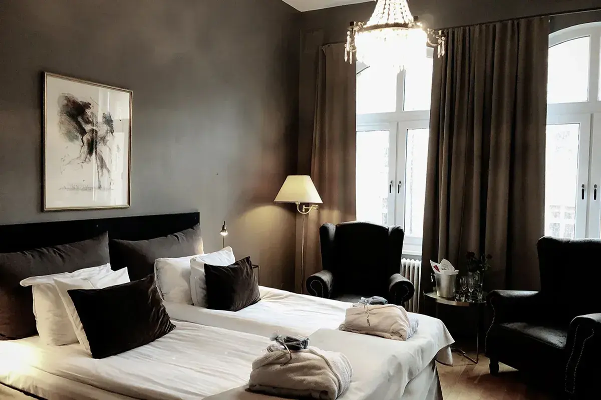 Ett elegant hotellrum med dubbelsäng, konst på väggen och en kristallkrona. Mysig hotellrum inredning med fåtöljer och en champagnehink.
