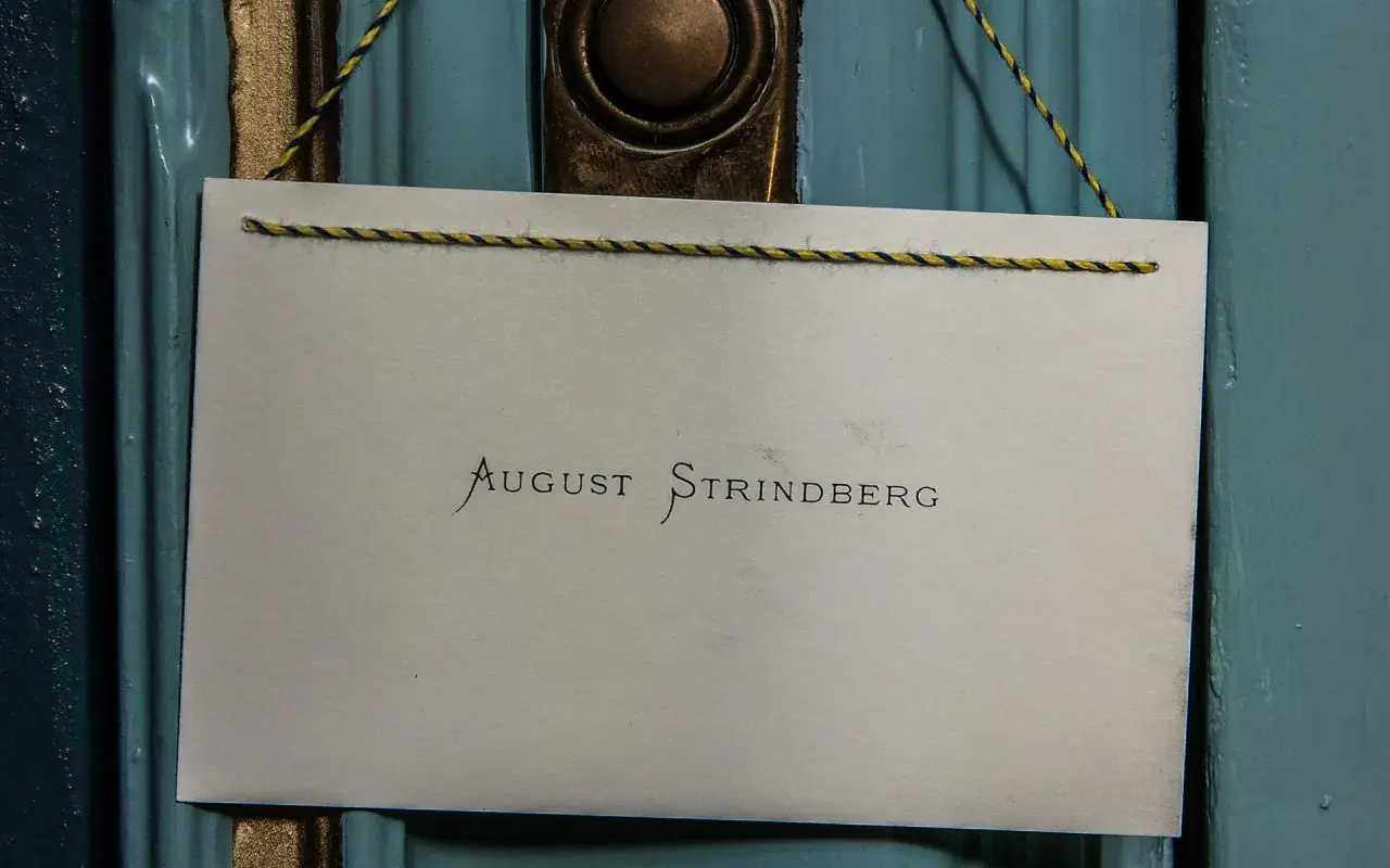 En skylt med texten "August Strindberg" hänger på en blå dörr, kanske vid Strindbergsmuseet.