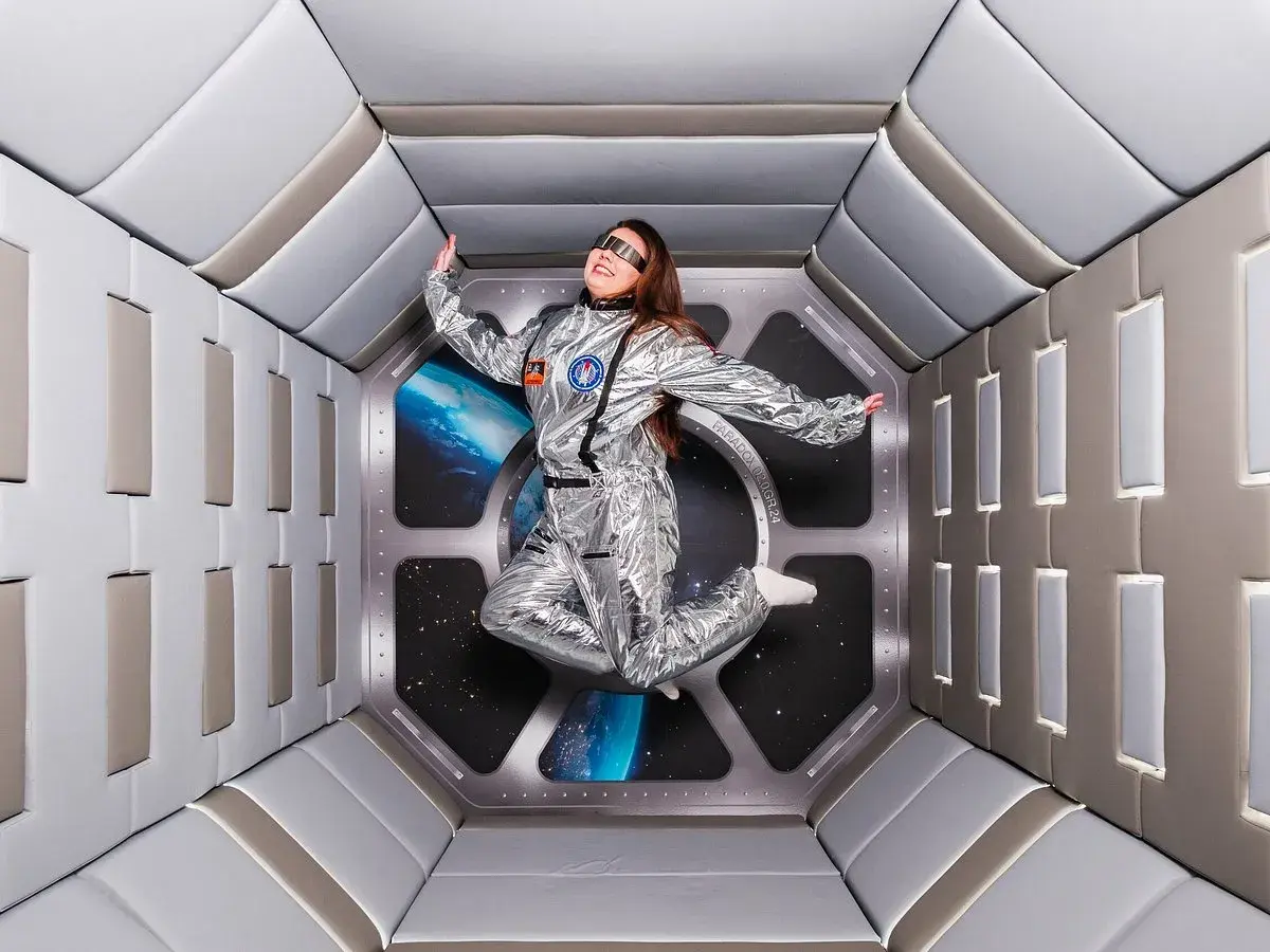 En person i rymddräkt svävar i en futuristisk tunnel, en del av en museum illusion i Stockholm.