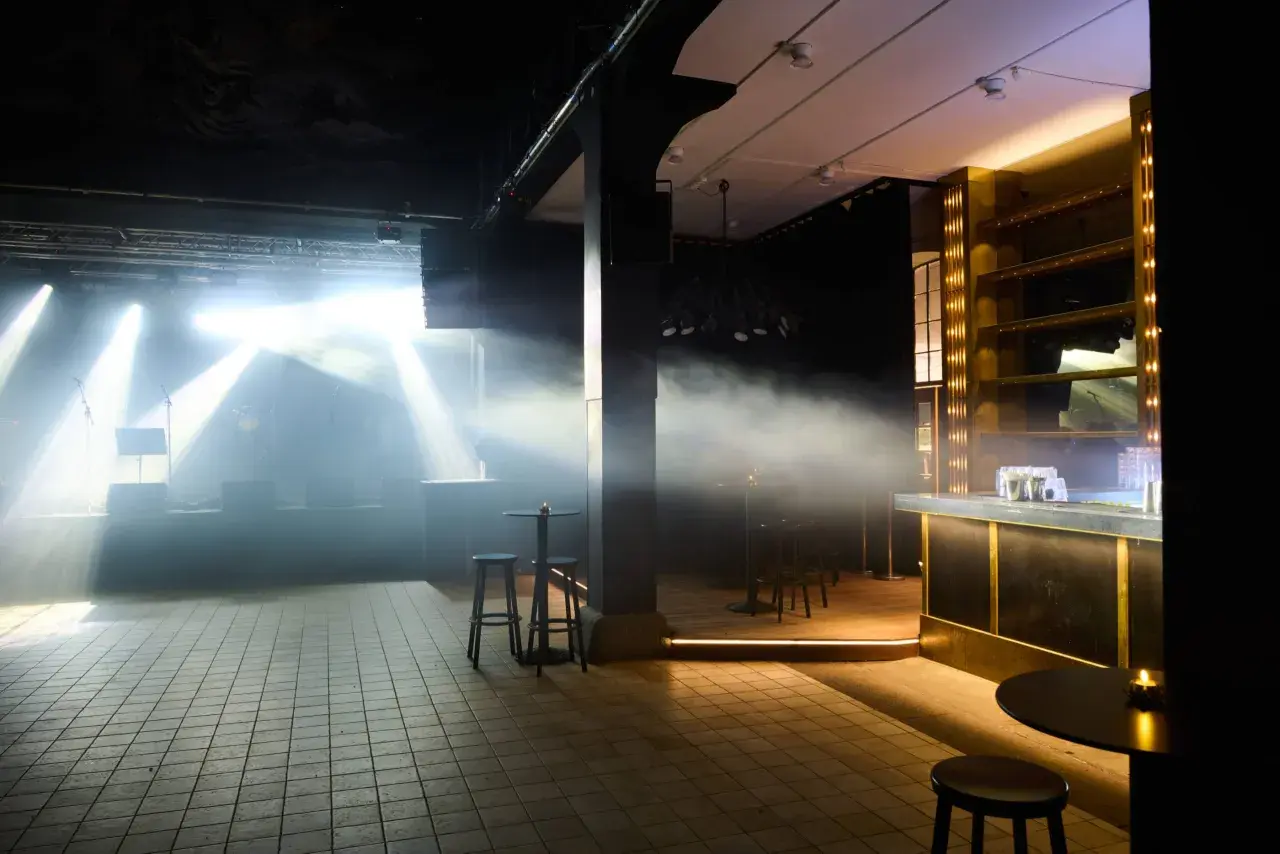 Scenljus och rök fyller lokalen på slaktkyrkan Stockholm. En bar i guld och svart syns till höger.