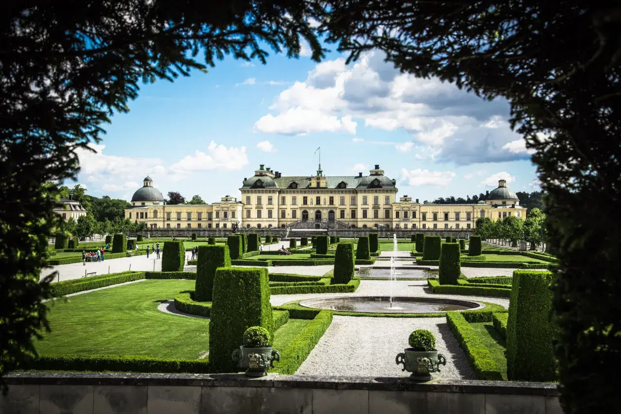 Drottningholms slottspark med fontäner och välklippta häckar. Kanske kungens båt ligger vid kajen, redo för en tur.