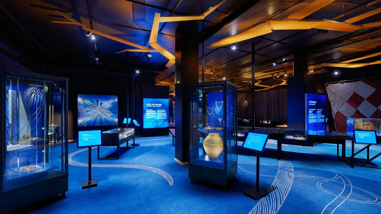 En utställning om historiska museet vikingar. Blå matta med vita mönster, montrar med föremål och skärmar med information.