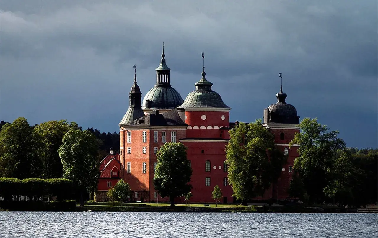 Mariefreds slott reser sig stolt vid vattnet, med sina röda tegelväggar och kupolformade tak under en dramatisk himmel.