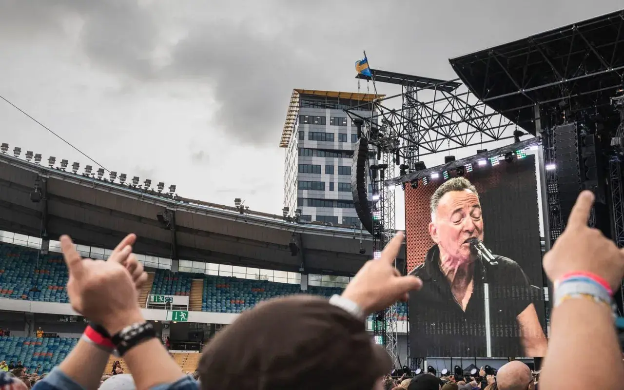 Publiken njuter av en Bruce Springsteen konsert i Sverige. En storbildsskärm visar The Boss sjunga medan fansen gestikulerar.