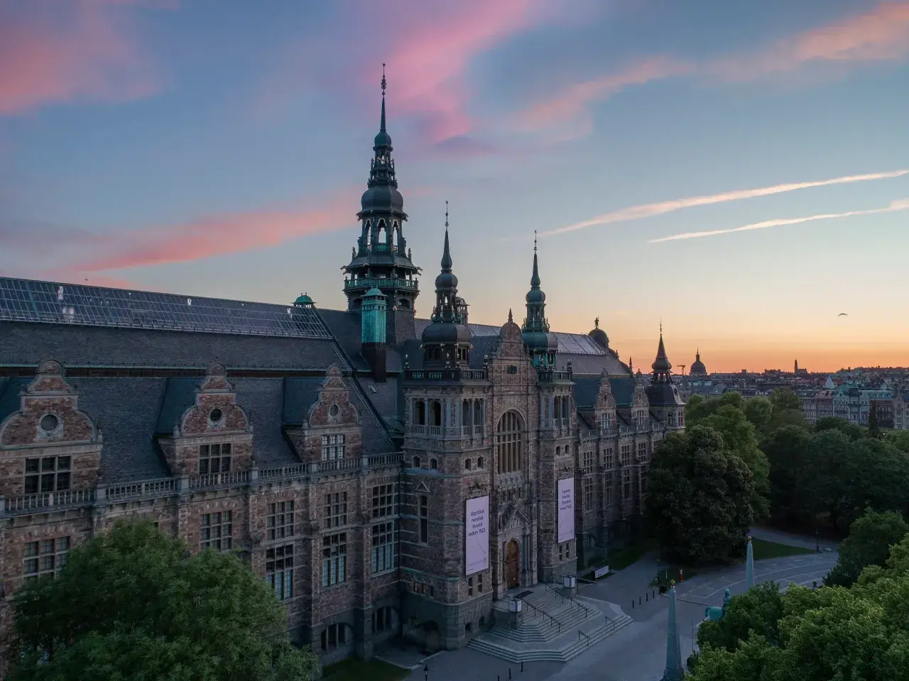 Nordiska museet badar i rosa kvällsljus. Imponerande arkitektur med torn och detaljer.