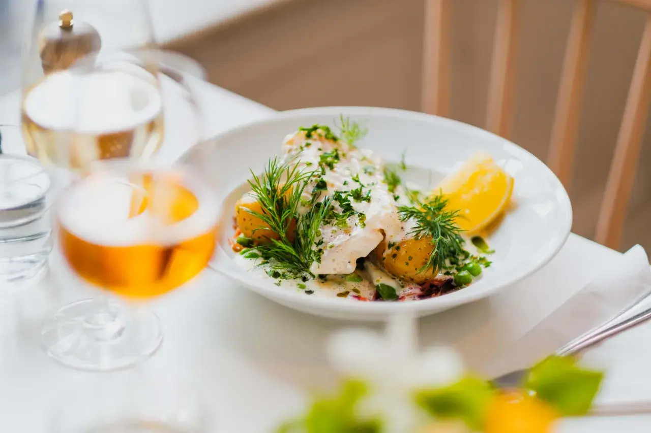 En vacker fiskrätt med potatis, ärtor och dill serveras på en vit tallrik. En perfekt måltid på Waldemarsudde restaurang.