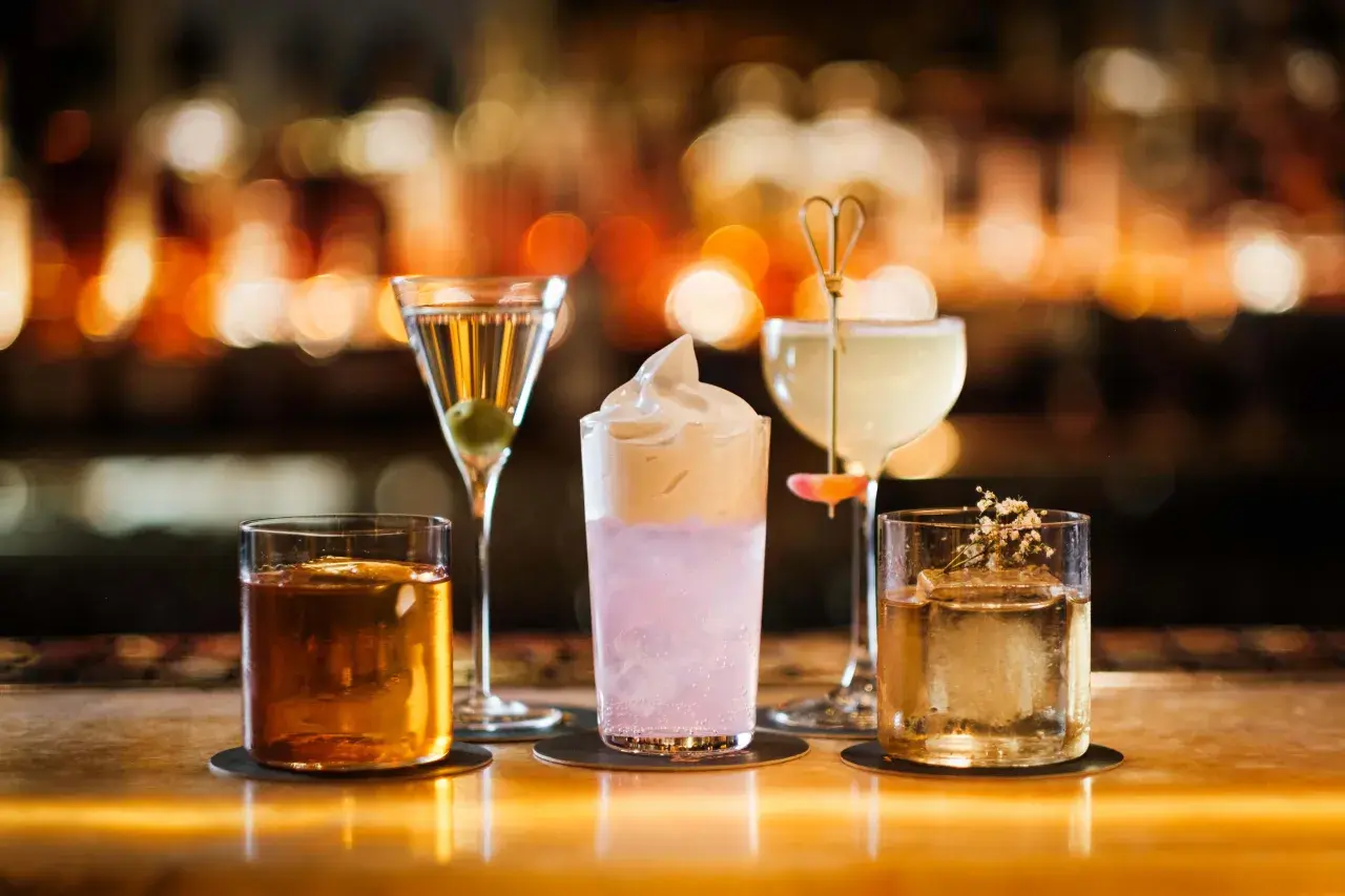Fyra drinkar på en bänk, en martini, en rosa drink med skum, en ljus drink med en blomma och en bärnstensfärgad drink. En perfekt kväll på Hallwylska bar.