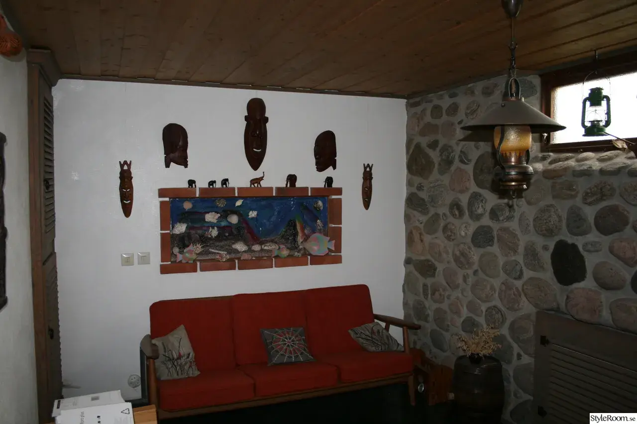 Gillestuga inspiration med en röd soffa, konstverk med afrikanska masker och stenklädd vägg.