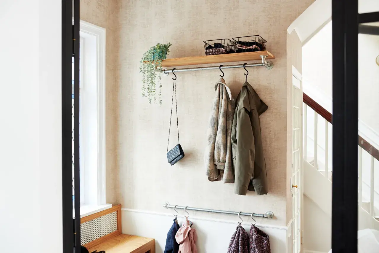Långsmal hall inspiration med klädhängare, hylla med korgar och en väska. En bänk i trä syns till vänster.