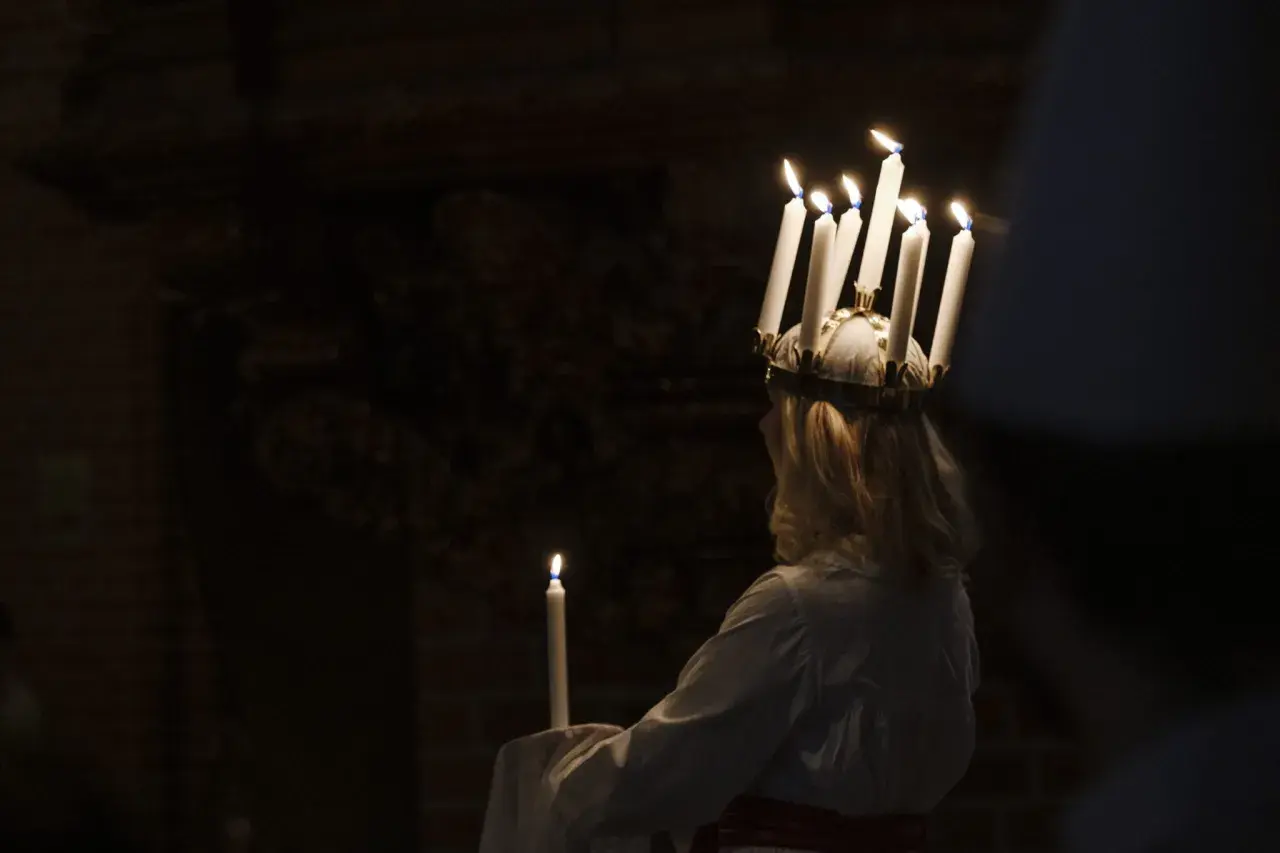 En flicka med ljus i håret, en traditionell Storkyrkan Lucia, håller ett ljus i mörkret.