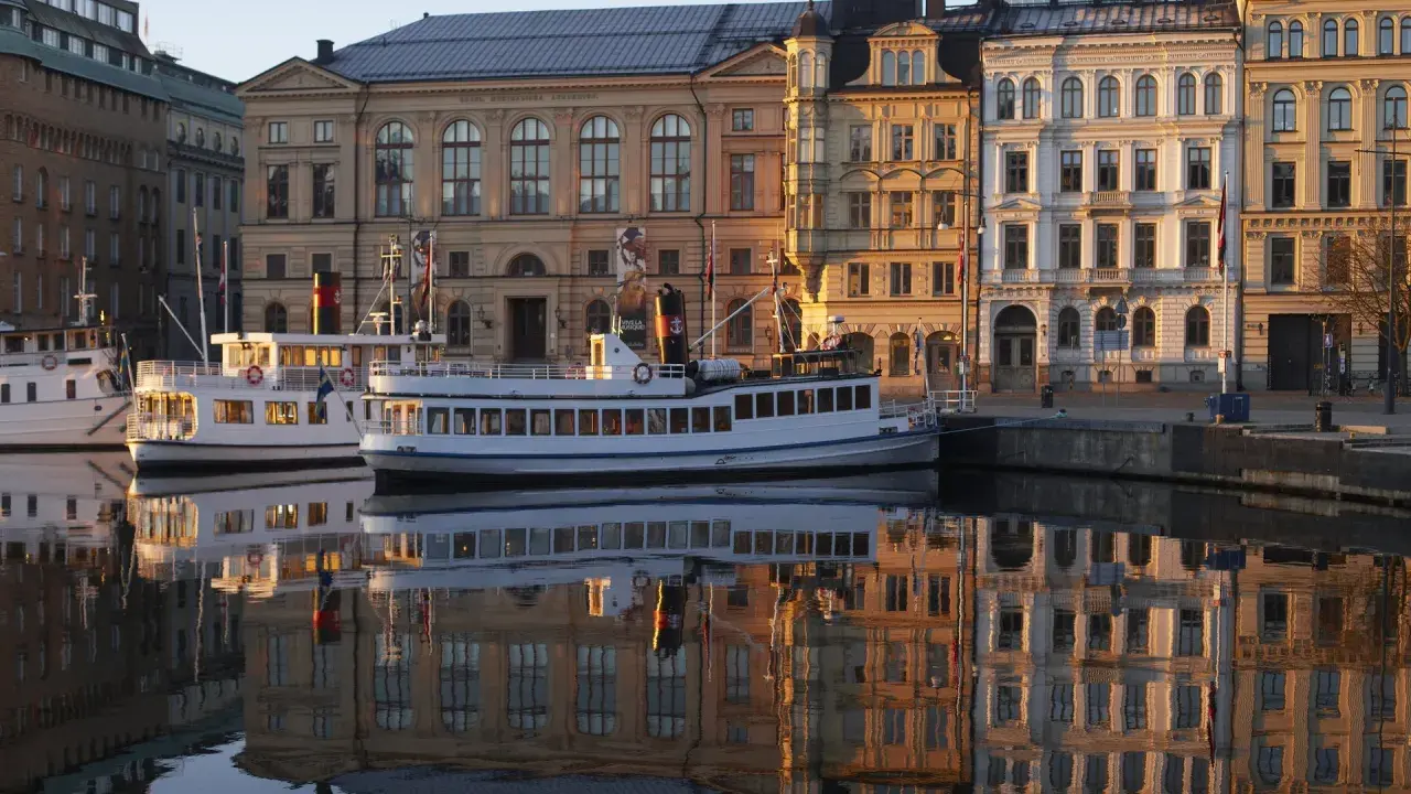 Fartyg i hamnen speglas i vattnet framför byggnader som vittnar om musikaliska Stockholm.