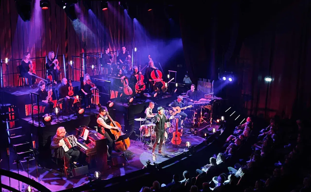En orkester spelar på en scen i Stockholm, med en sångare i förgrunden. En levande revyupplevelse.