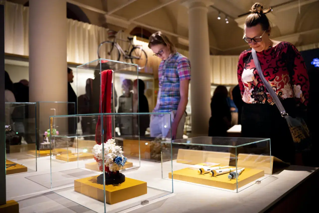 Besökare på muzeum nobla beundrar utställningar i glasmonter, inklusive en röd scarf och molekylmodeller.