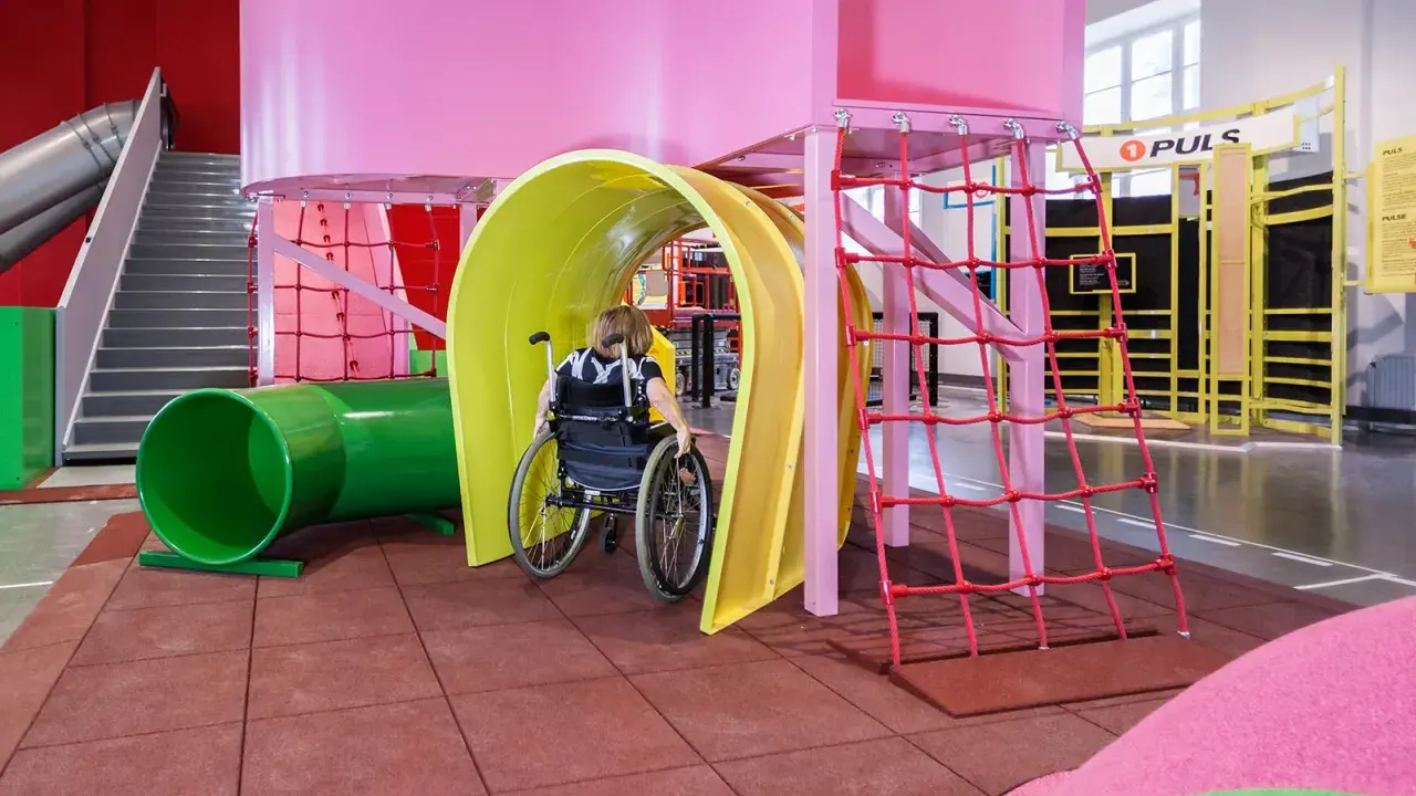 En person i rullstol navigerar genom en färgglad lekplats på Teknikmuseet Stockholm.
