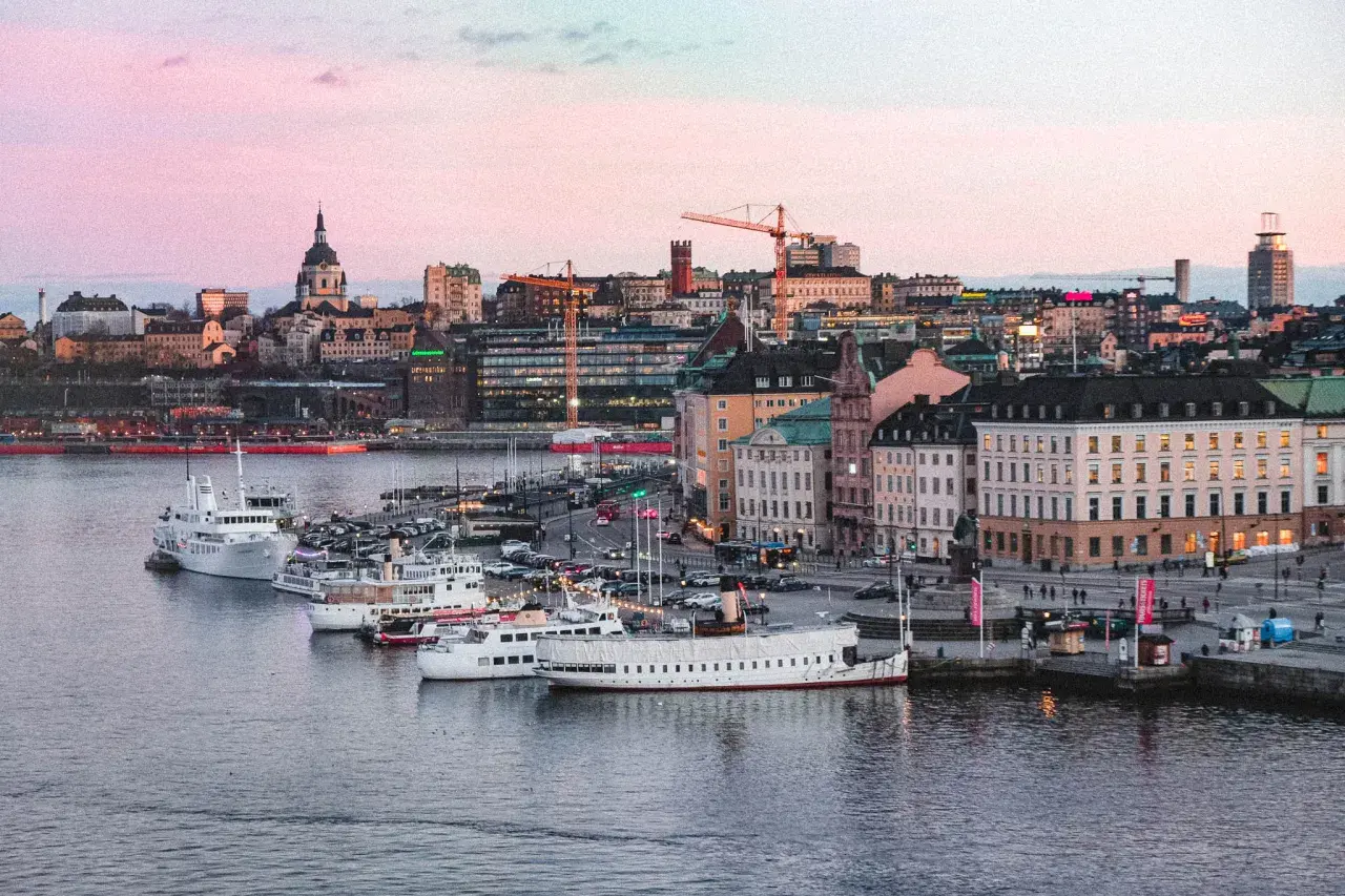 Vackert ljus över vattnet och båtar vid kajen i Stockholm. Staden ser inbjudande ut, redo för äventyr imorgon.