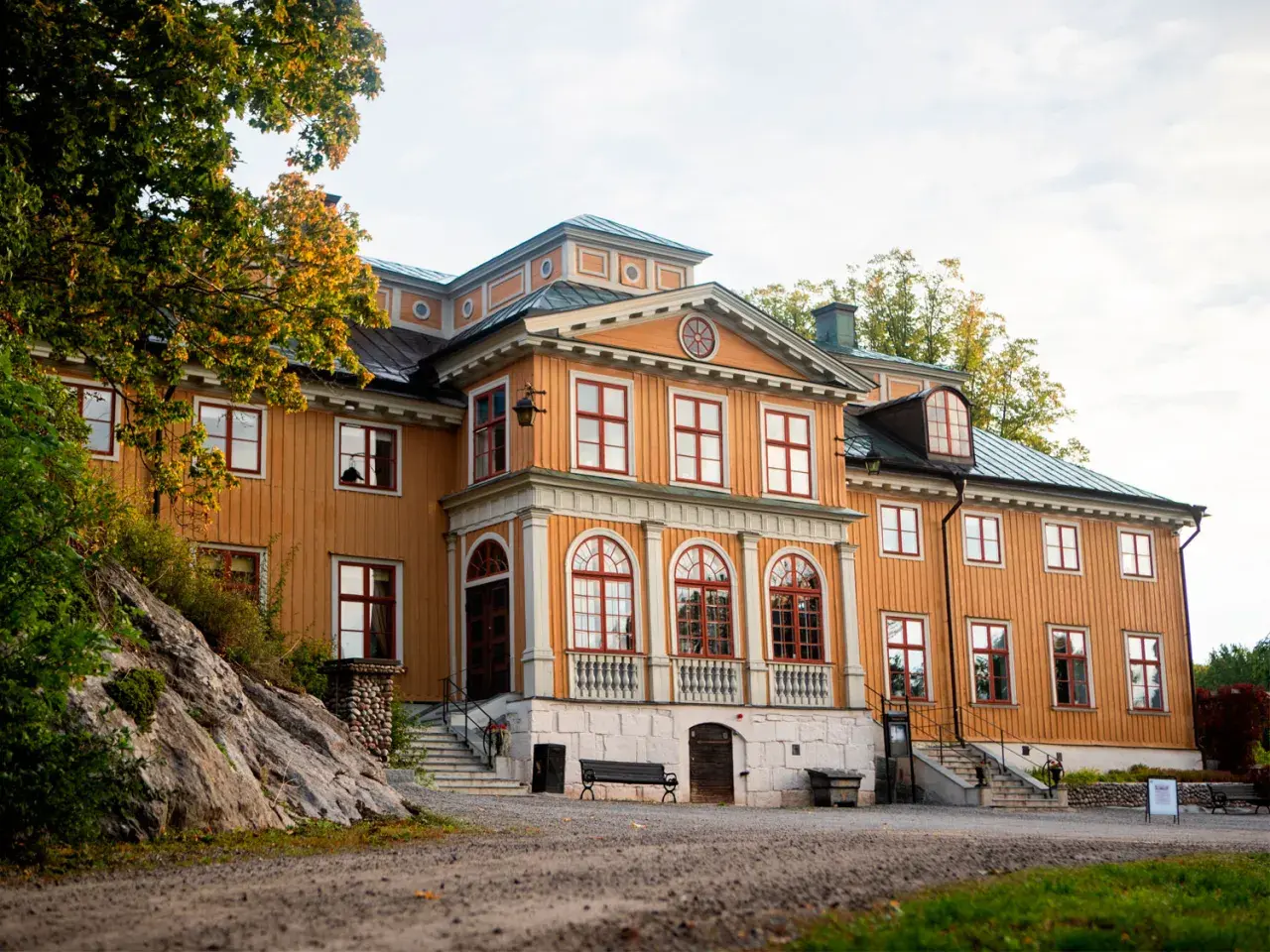 Vackert gul träbyggnad med röda fönster och tak, Rastaborgs slott, omgivet av höstfärgad grönska.