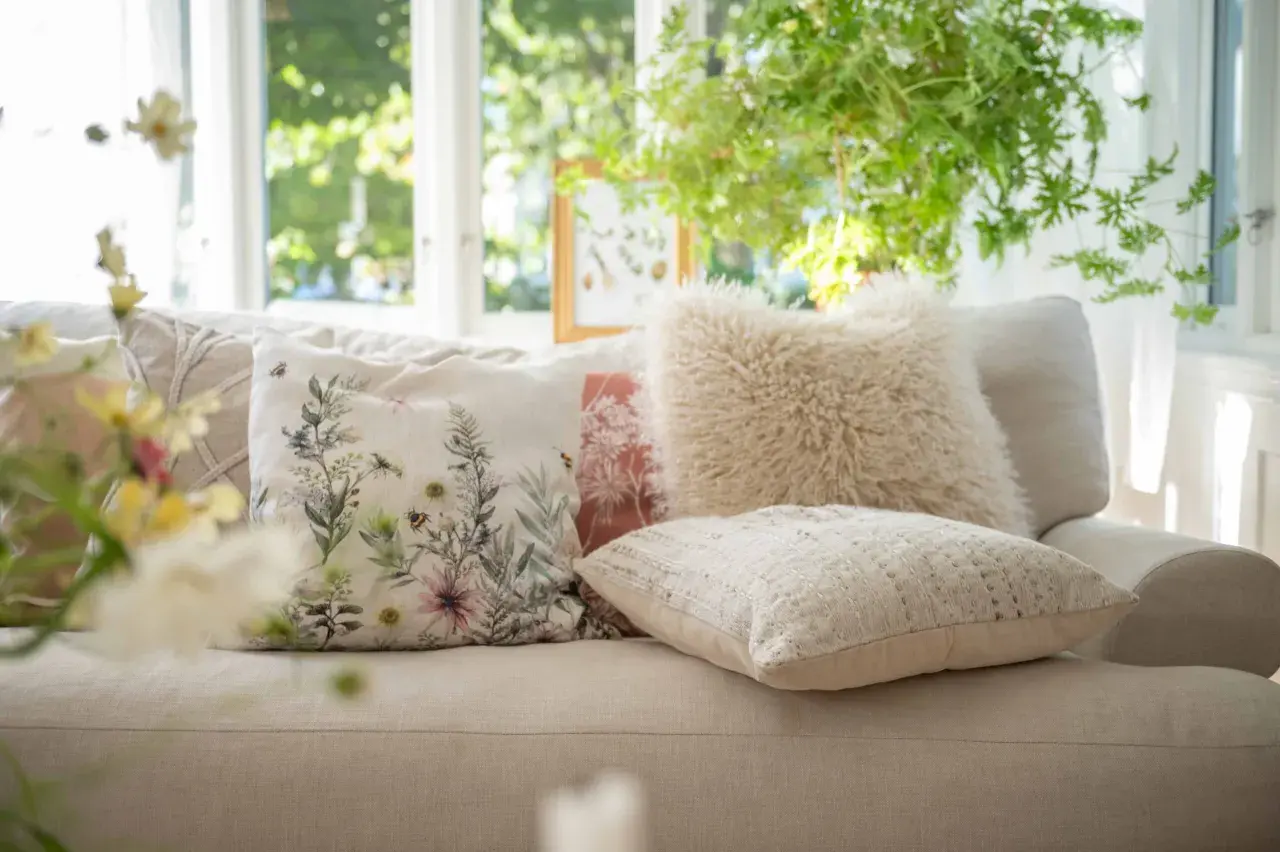 Mysiga kuddar i soffan inspiration: en blommig kudde med bin, en fluffig beige kudde och en texturerad ljus kudde skapar en ombonad känsla.
