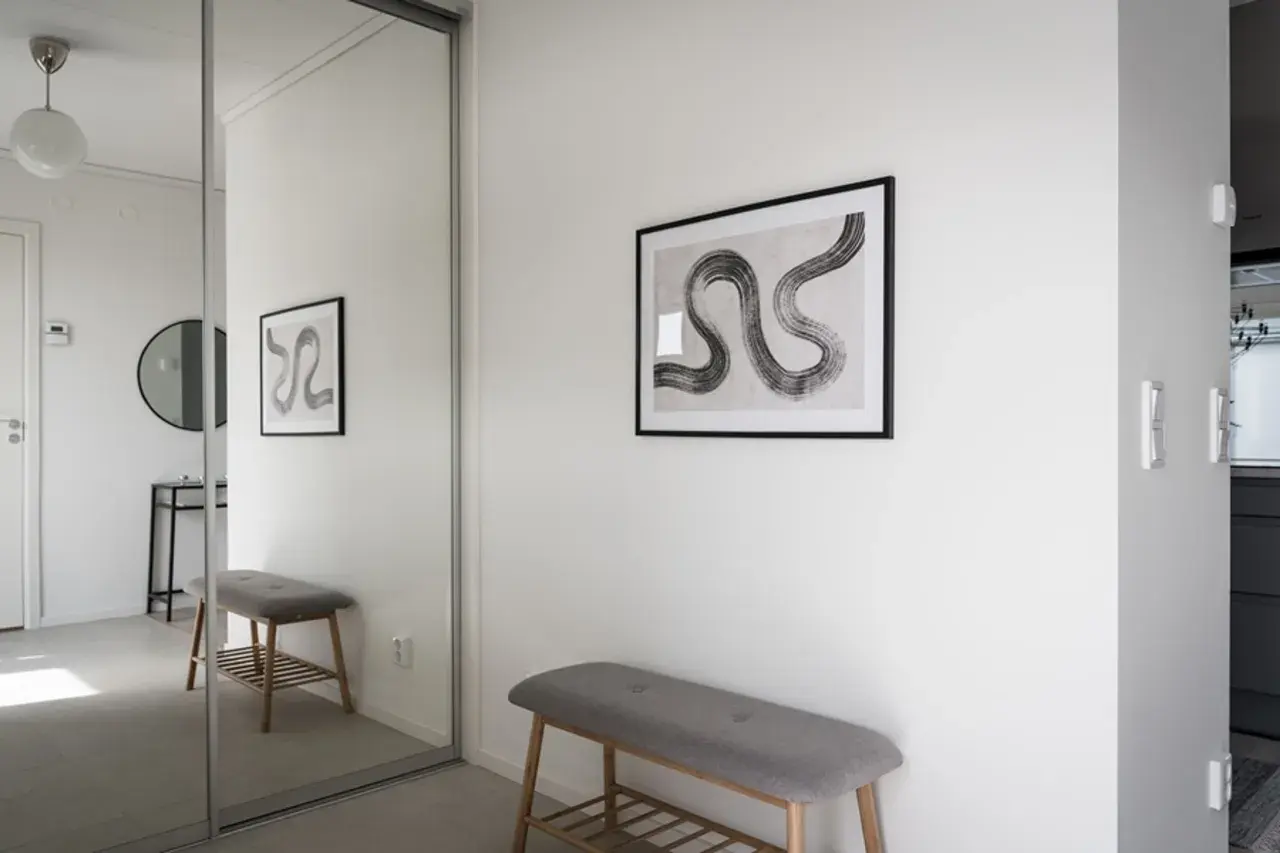 En hall med en grå bänk och en spegelvägg. Konst på väggen ger hall inspiration.