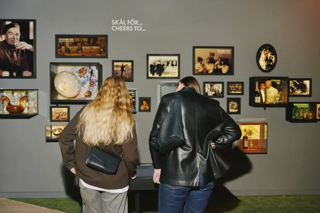 Två besökare studerar utställningen på sprit museum. Väggen är täckt av bilder och föremål som skildrar olika traditioner och högtider.
