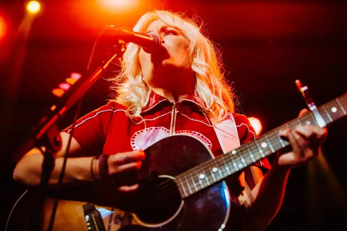 Maja Francis sjunger och spelar gitarr under en konsert, upplyst av rött scenljus.