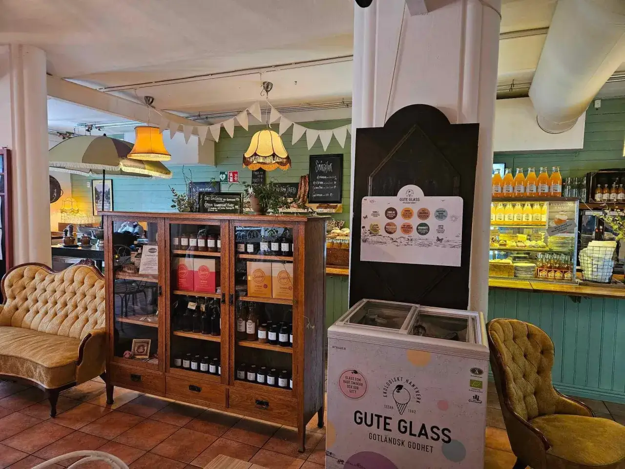 Mysigt café med en gul sammetssoffa, ett vitrinskåp fyllt med godsaker och en frys med