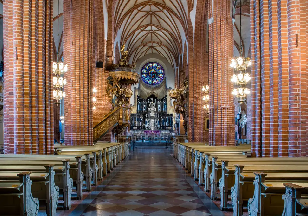 Interiör av Storkyrkan i Gamla Stan, Stockholm. Långa bänkrader leder mot altaret under ett valv.