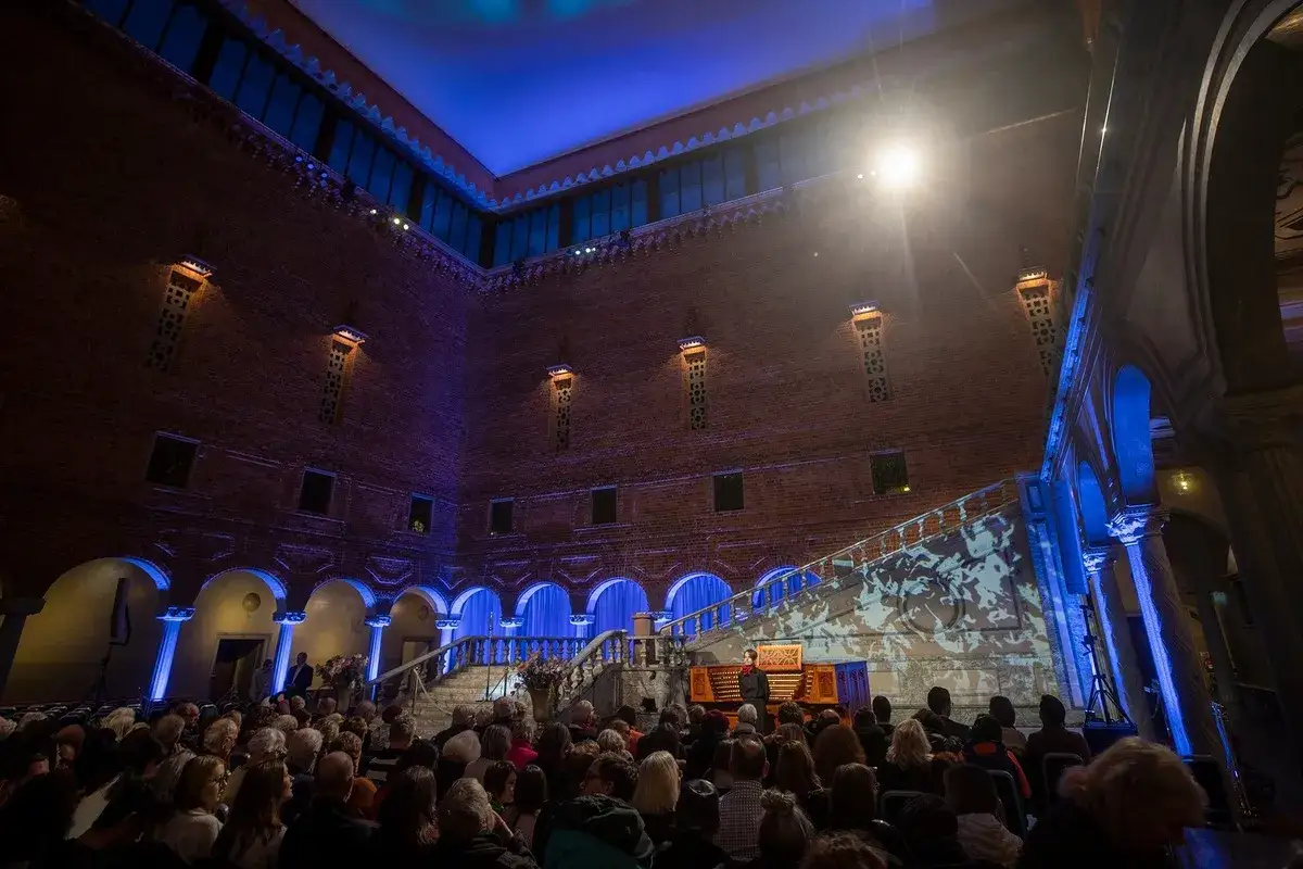 Publik njuter av en nyårskonsert i Stockholm. En organist spelar i en vacker tegelbyggnad med blå belysning.