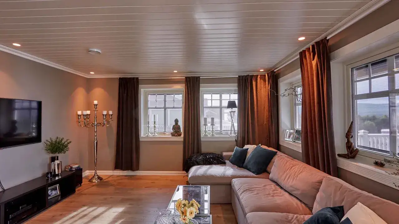 Ett stort vardagsrum med en bekväm soffa, TV, ljusstakar och fönster med bruna gardiner.