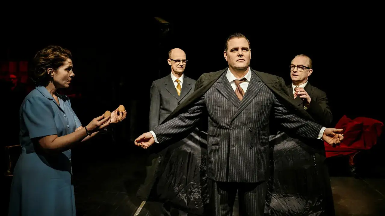 Scen från kulturhuset teater: en kvinna med ägg i handen, en man i randig kostym och två män i bakgrunden.