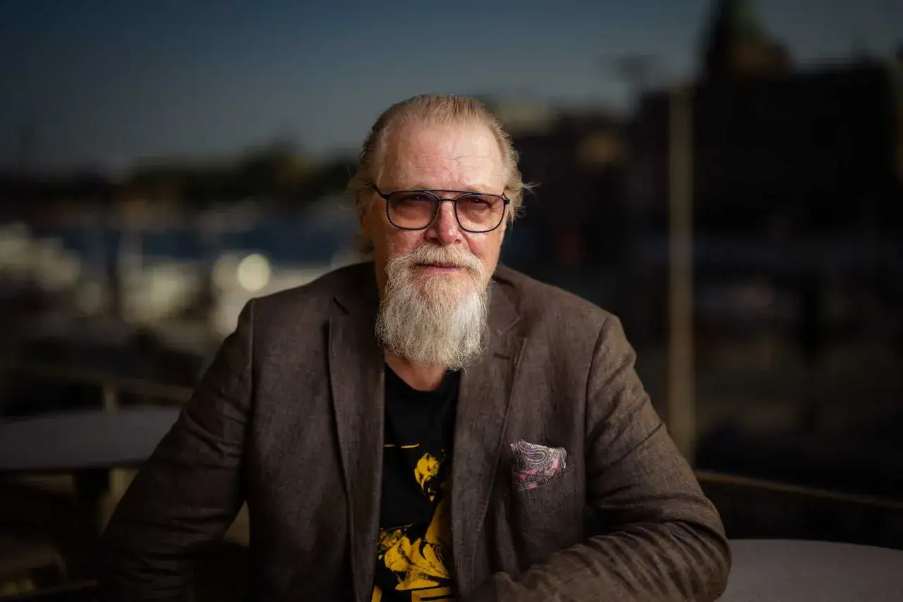 Äldre man med vitt skägg och glasögon, klädd i kavaj. Kanske redo att spela Kung Lear på Dramaten?