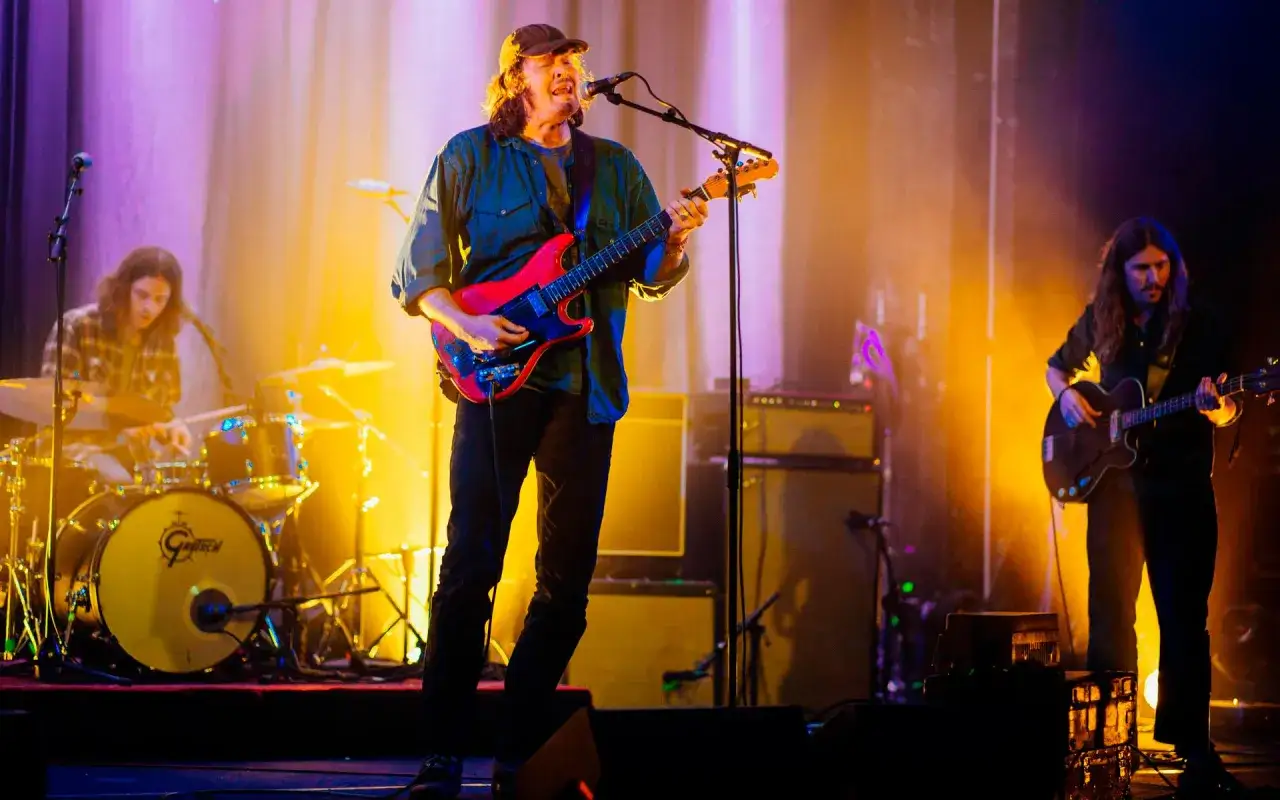 Daniel Norgren konsert med bandet. Sångaren spelar gitarr, en trummis syns i bakgrunden och en basist till höger.