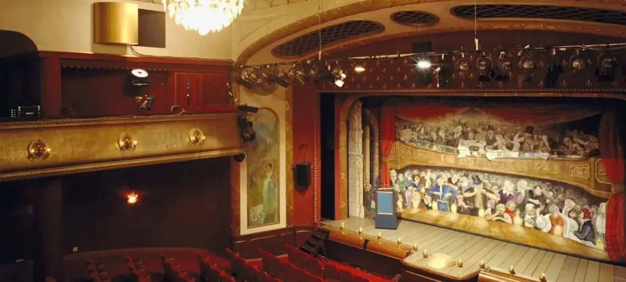 Teater Odenplan med sin pampiga scenmålning av publik i loger. Röda sammetssoffor och gyllene detaljer skapar en klassisk atmosfär.
