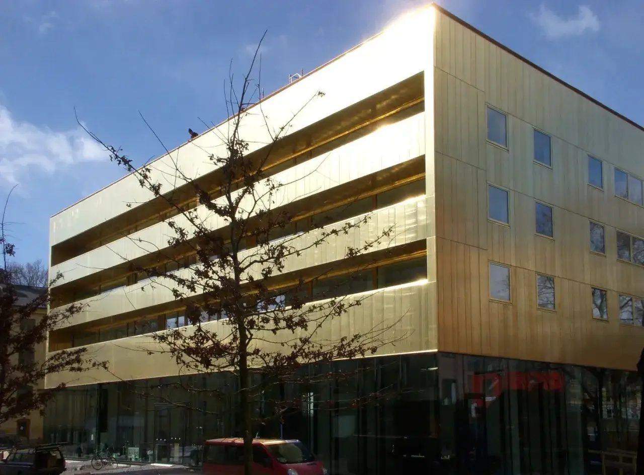 Modern byggnad med guldfasad, likt ett museum i Vasaparken. Solen reflekteras i fasaden.