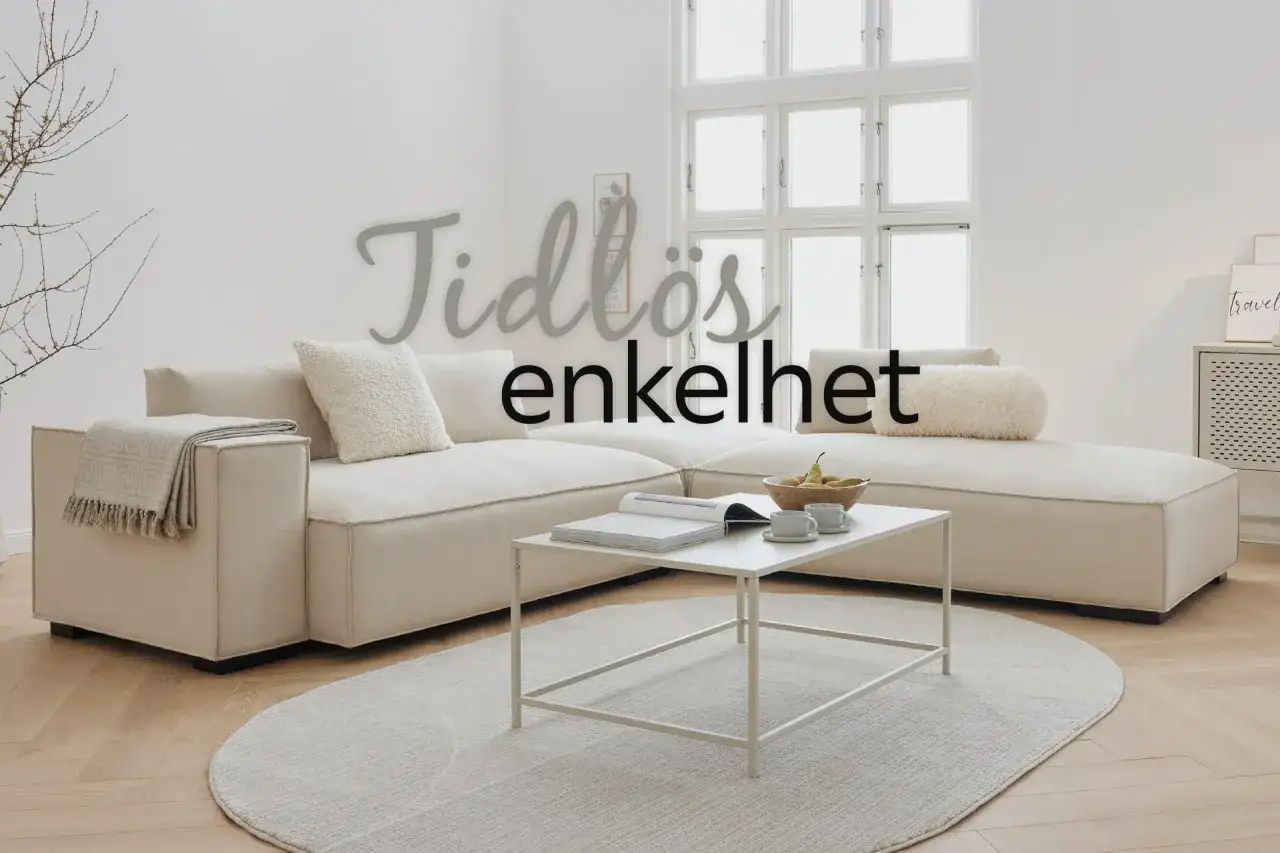 Tidlös enkelhet i ett ljust vardagsrum med en stor, beige soffa, ett vitt soffbord med böcker och fruktskål, samt en rund matta. Vit inredning inspiration.