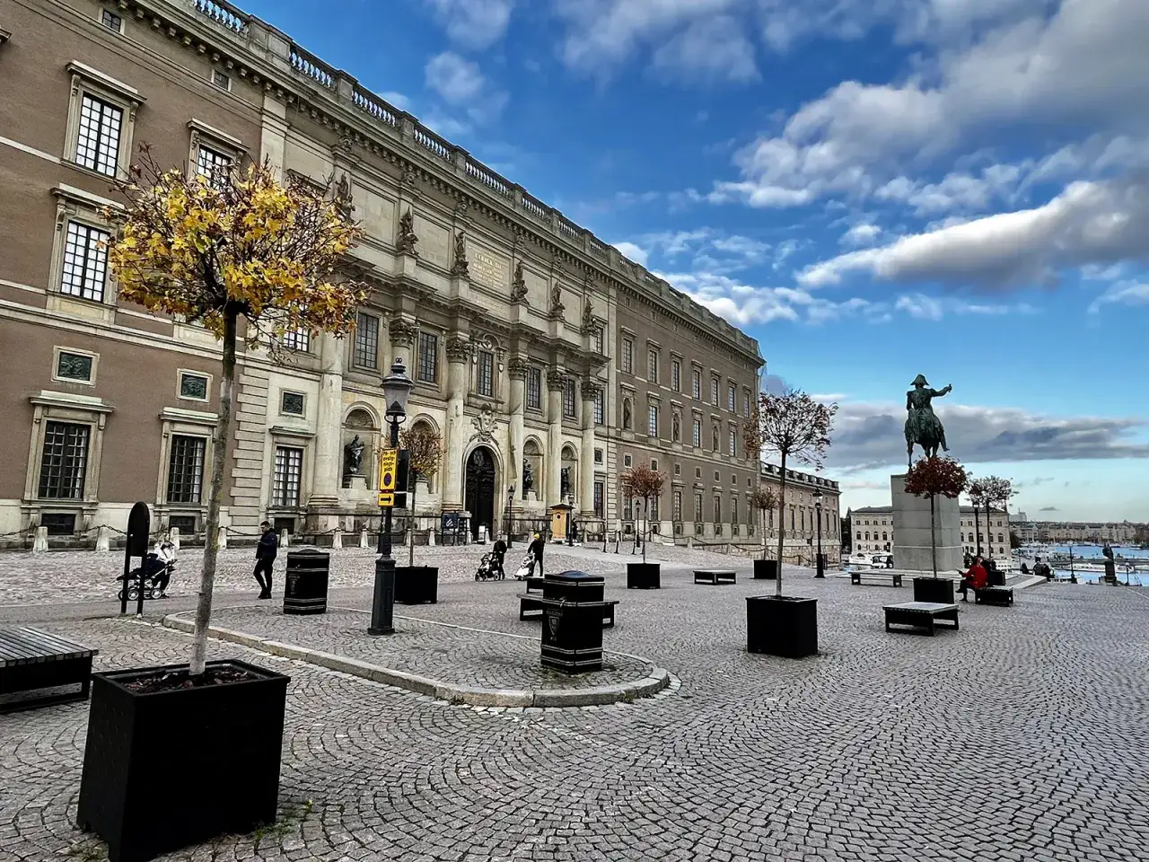 Stora torget framför slottet i Gamla Stan, Stockholm, med en ryttarstaty och höstträd under en molnig himmel.