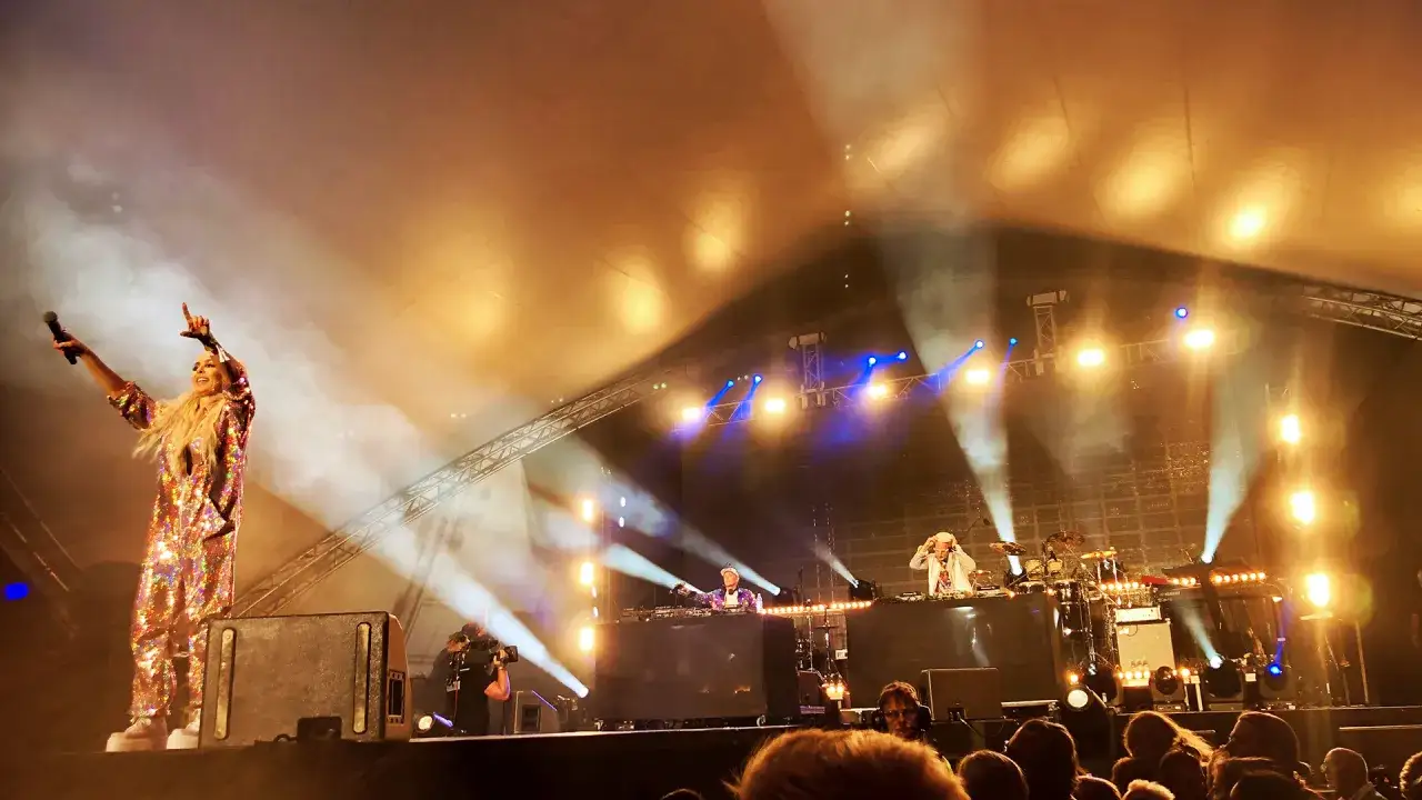 En kvinna i glittrig dräkt sjunger på scen, omgiven av rök och ljus. En del av en svenska artister lista på en stor konsert.