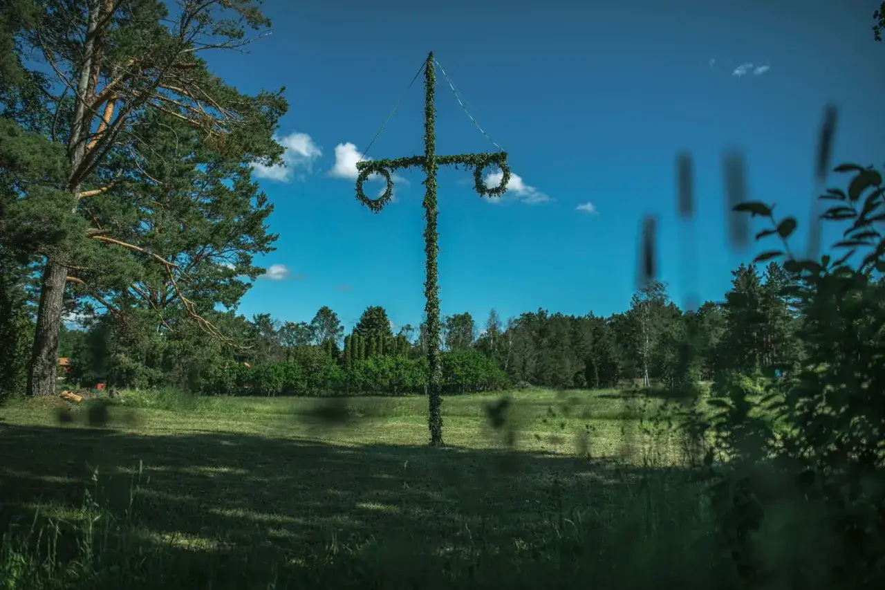 En midsommarstång på Mosebacke, klädd i grönt, väntar på firandet under en klarblå himmel med moln.