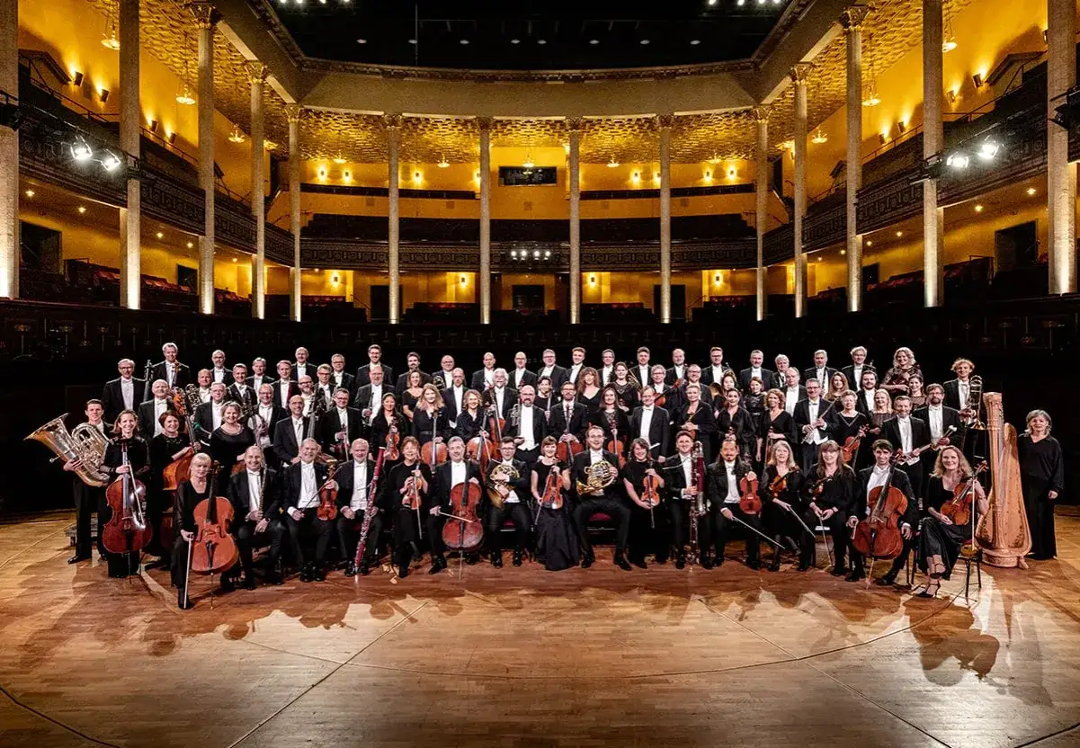 Stockholms filharmoniker poserar med sina instrument i en storslagen konsertsal.