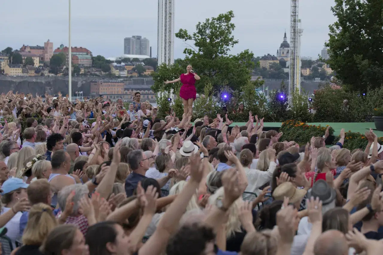 En sångerska i en rosa klänning uppträder på en scen under en konsert på Skansen. Publiken jublar och höjer händerna.