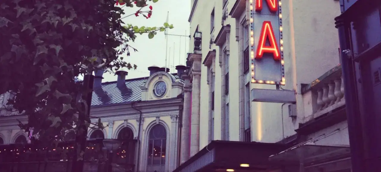 Neonskylt lyser upp fasaden vid China Teatern Stockholm. Träd med blommor skymtar till vänster.