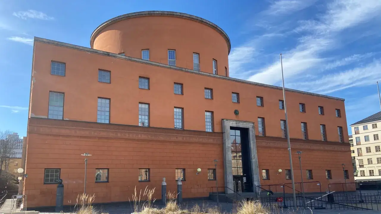 Stockholms kulturhus, en ikonisk orange byggnad med en rundad överdel, står stolt under en blå himmel med moln.