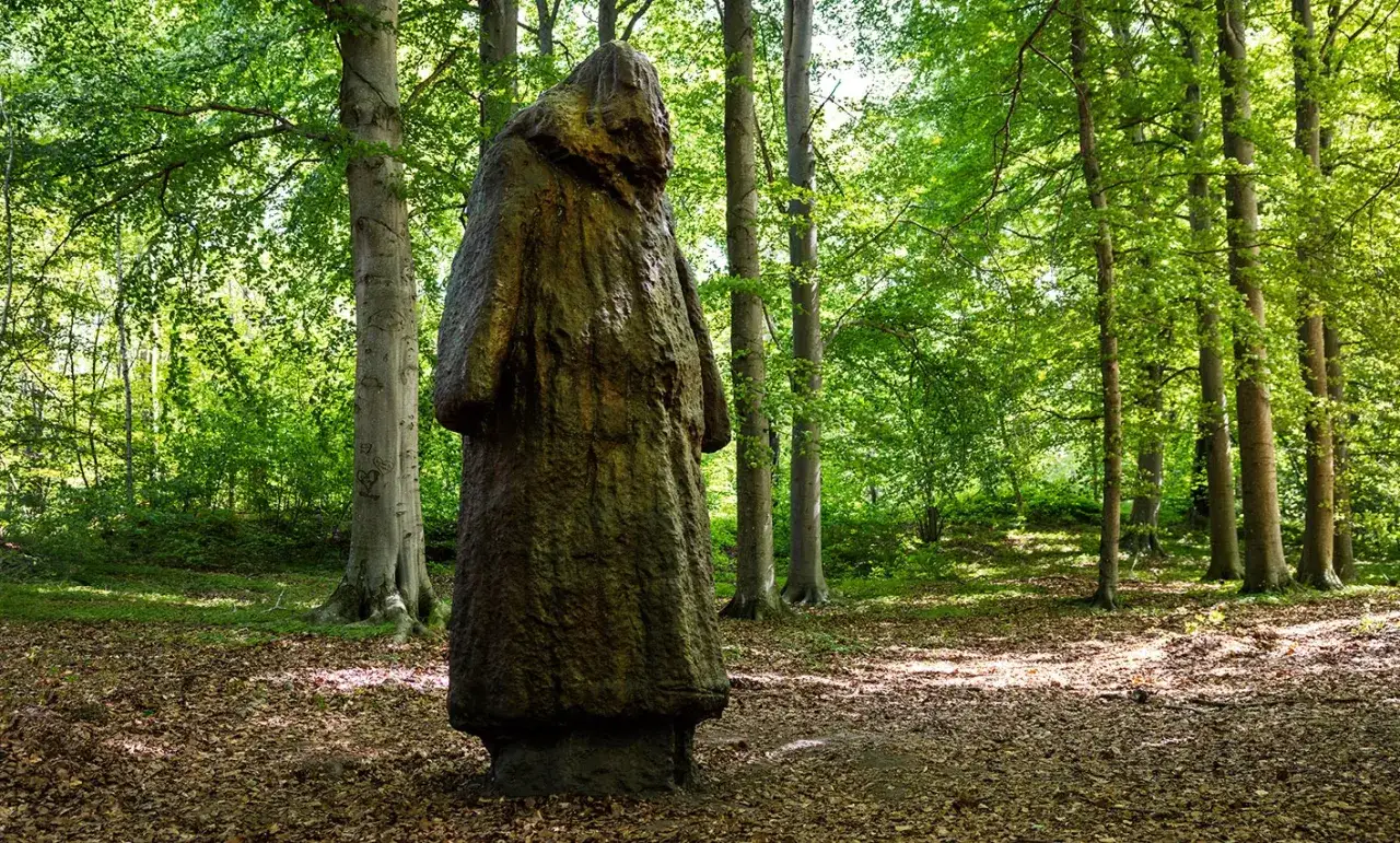 En mystisk figur står i en lummig skog. Estelles skulpturpark bjuder på konst i naturen.